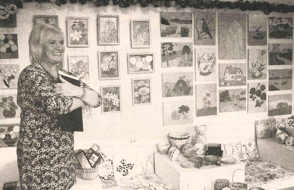 Pasākuma vadītātāja Sanita Eglīte pie projekta dalībnieku - “Saulstariņu” un senioru izstādes. Attēls: Malienas Ziņas, 2011. gada 29. oktobris.